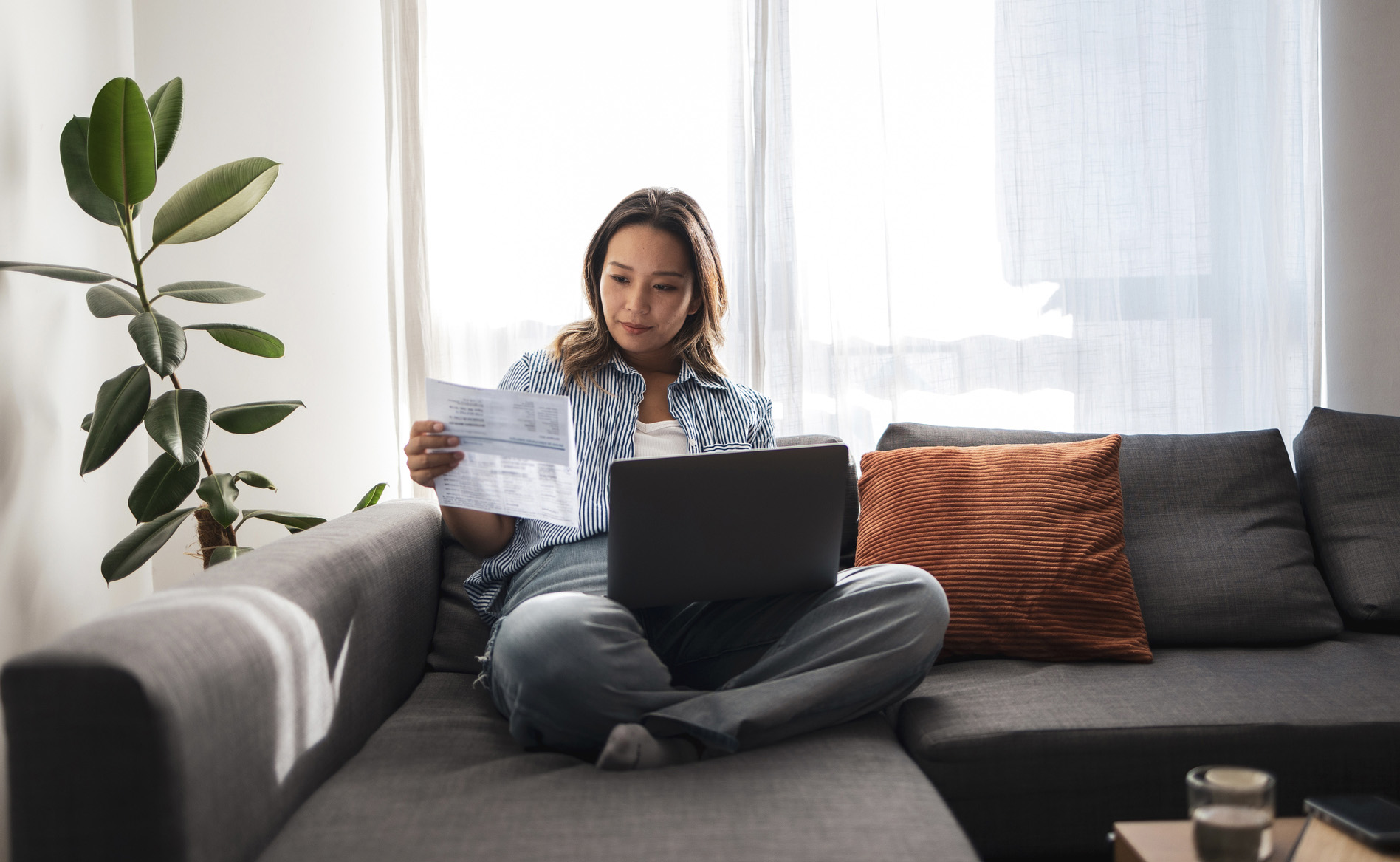 Asian woman analyzing documents while working on laptop from home